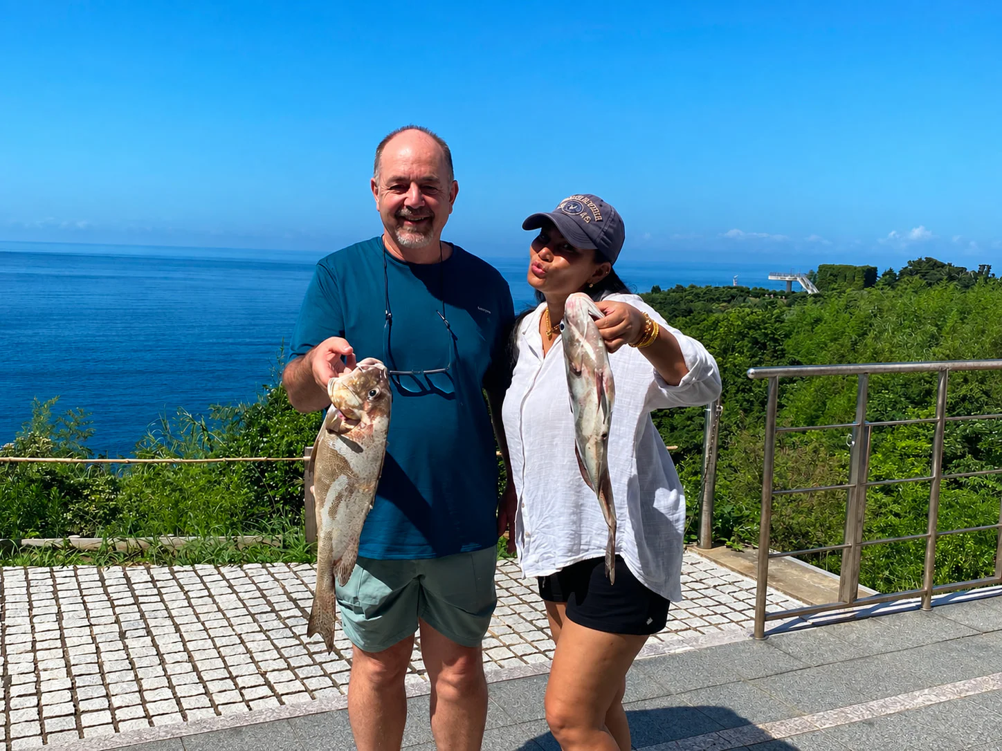 海辺で釣った魚を手に笑う二人
